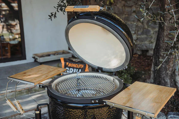 Monolith ONE premium kamado grill with open lid and bamboo side shelves.