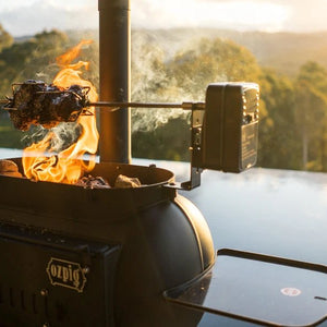 Ozpig Cooker & Heater with rotisserie grilling by a scenic poolside.
