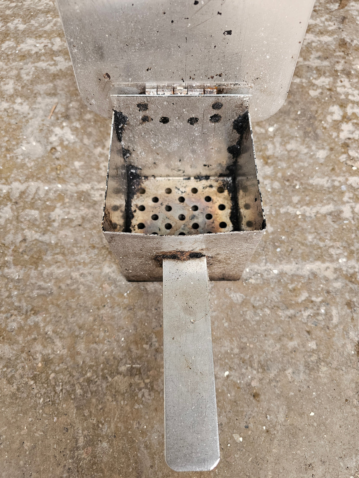 Metal smoker part with burn marks on concrete
