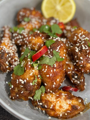 Spicy chicken wings garnished with sesame seeds, red chili, and cilantro, flavored with Caribbean Mango Hot Sauce. Served with lemon slice.