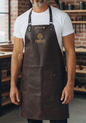 Leather BBQ Apron - Jack the Ripper by FireFly Barbecue shown worn, featuring premium brown leather with copper embossed logo and front pockets.