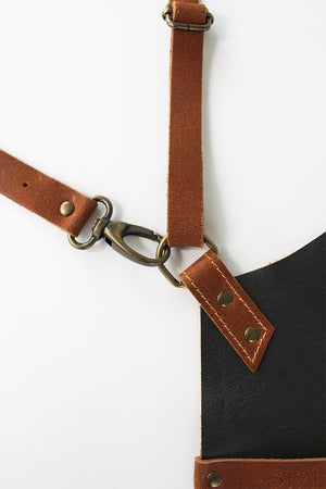 Adjustable leather strap system on the BBQ apron with brass hardware, emphasizing durability and ergonomic design for grilling comfort.