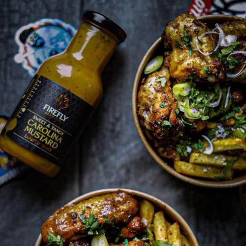 Firefly Carolina Mustard BBQ Sauce bottle next to grilled chicken wings and fries, highlighting its use in Southern-style BBQ dishes.