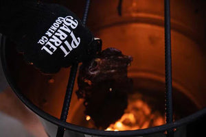 Close-up of Pit Barrel Pit Gloves - FireFly Barbecue in action, gripping meat over open flame in a smoker, ideal for high-heat outdoor cooking.