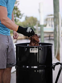Griller wearing Pit Barrel Pit Gloves - FireFly Barbecue while handling meat in a Pit Barrel Cooker, perfect for safe and stylish BBQ handling.