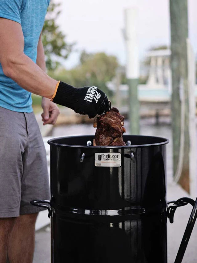 Griller wearing Pit Barrel Pit Gloves - FireFly Barbecue while handling meat in a Pit Barrel Cooker, perfect for safe and stylish BBQ handling.