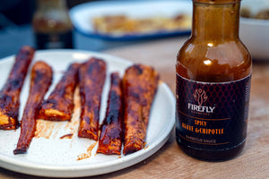 Spicy Agave & Chipotle BBQ sauce bottle next to grilled vegetable ribs, highlighting vegan-friendly Firefly BBQ Hot Agave Nectar.