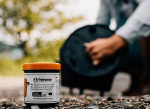 Petromax Care Conditioner for Cast and Wrought Iron placed outdoors with a person applying it to a Dutch oven, essential for cast iron maintenance.