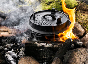 Petromax 1.6L Cast Iron Dutch Oven in use over open flames and wood fire, designed for rugged outdoor cooking and grilling.