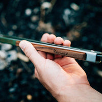 Person holding stainless steel BBQ tongs with wooden handle outdoors