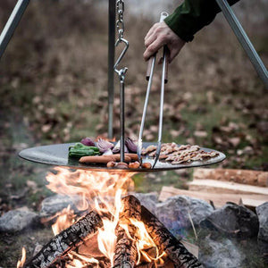 Petromax BBQ and Coal Tongs - Small in use over an open fire pit, flipping food on a suspended grill, perfect for outdoor Dutch oven setups.
