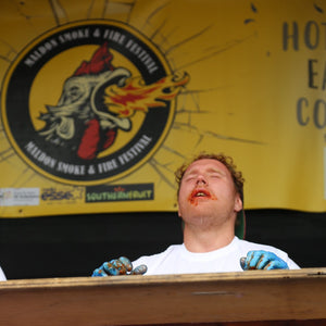 Participant overwhelmed by heat during hot wings eating contest featuring 7 Deadly Wings Hot Sauce at Maldon Smoke & Fire Festival.