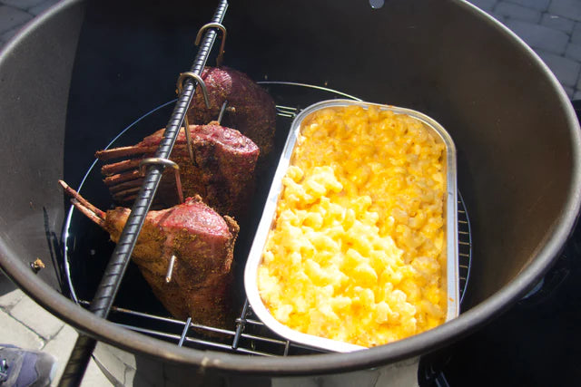 Pit Barrel Hinged Grate in action with smoked lamb and mac and cheese tray, showing multi-zone cooking in outdoor drum smoker.