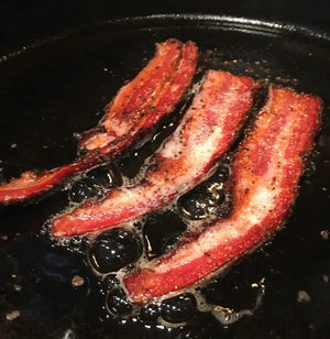Crispy fried bacon strips in a skillet, made using the Sweet Rosemary & Thyme Bacon Cure, highlighting its rich flavor and texture.