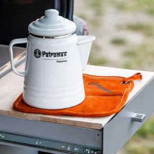 Petromax Aramid Pro 300 Potholder used as a heat-resistant mat under a white enamel kettle, suitable for outdoor kitchen setups.