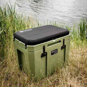 Petromax Seat Cushion on green kx50 cool box by a lake, ideal for fishing, camping, or outdoor adventures.