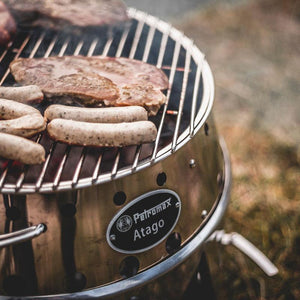 Close-up of Petromax Atago grill with sausages and steak cooking, emphasizing its use as a high-performance BBQ stove.