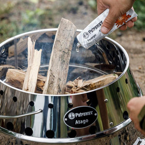 Petromax Atago fire pit being ignited with wood and fire starter, showcasing its use as a wood fired stove for outdoor cooking.