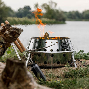 Petromax Atago in fire pit mode with visible flames, ideal for outdoor warmth and cooking in camping or garden settings.