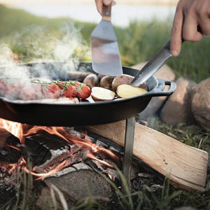 Petromax Flexible Spatula with Long Handle used to cook vegetables and meat in a Dutch oven over an open flame, perfect for outdoor grill setups.