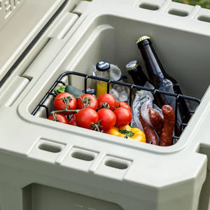 Petromax Dry Rack Basket inside a beige cool box, holding tomatoes, sausages, and drinks above ice for optimal freshness.