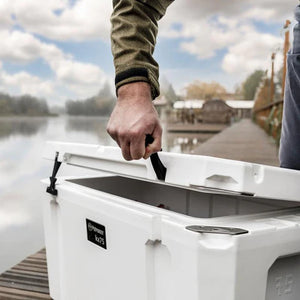 Person opening Petromax 75L Cool Box on a dock, showcasing its rugged build for outdoor food and drink cooling.