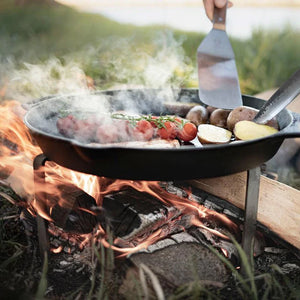 Petromax Cooking Stand holding a Dutch oven skillet with vegetables over an open fire, perfect for outdoor grilling and camping.
