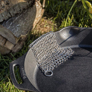 Petromax Chain Mail Cleaner resting on a cast iron Dutch oven outdoors, demonstrating its use for grill and campfire cookware cleaning.