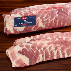 Uncooked Swift Brand USDA St Louis Ribs displayed on a wooden surface, showing marbling and hand-trimmed quality cuts.