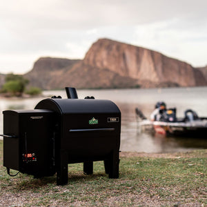 Green Mountain Grills TREK PRIME 2.0 Pellet Grill in scenic outdoor setting near water, emphasizing its mobile grilling features.