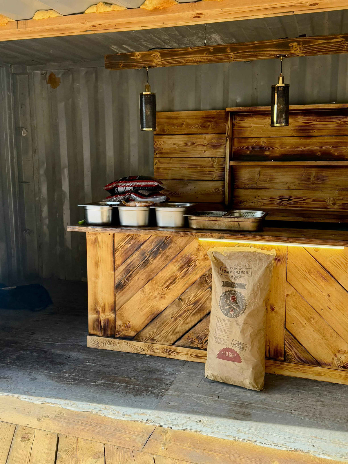 Wooden outdoor kitchen with bags of lump charcoal and grilling accessories