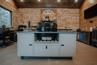 Indoor kitchen with brick wall, neon BBQ sign, and Primo grill