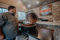 Man grilling steaks on Primo Kamado Charcoal Grill indoors, highlighting its use in professional BBQ settings.