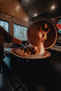 Primo Kamado Charcoal Grill in action with flames searing meat, showcasing high-heat ceramic grilling performance.