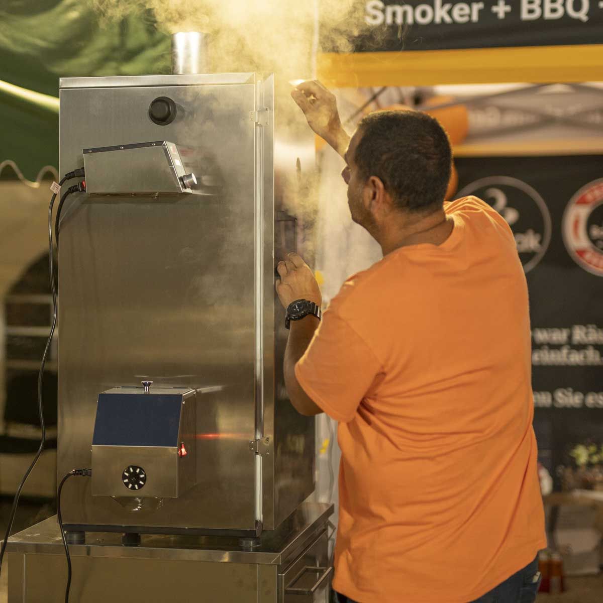 Man operating commercial stainless steel smoker at outdoor event