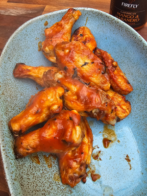 Chicken wings coated in Caribbean Mango Hot Sauce on a blue plate. Showcases the sauce’s glossy texture and tropical heat for BBQ meals.