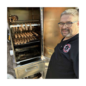 Man using Borniak Food dryer fan in smoker chamber filled with sausages, demonstrating quick meat drying for outdoor barbecue preparation.