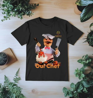 Mens Swedish Chef T-shirt in black laid flat on wooden surface, showcasing vibrant chef print and sustainable organic cotton fabric.