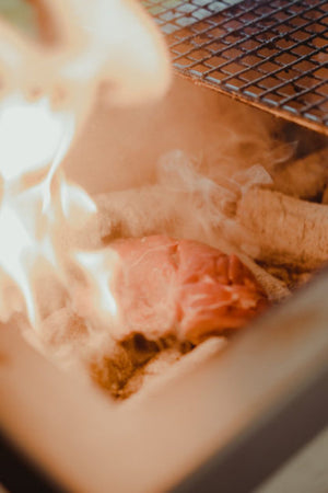 Close-up of meat grilling over charcoal inside the Kasai Extra Long BBQ Grill S/S, highlighting its high-heat cooking performance.