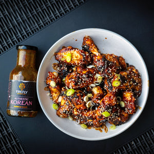 Bowl of grilled chicken wings glazed with Firefly Korean BBQ Sauce, garnished with sesame seeds and scallions for a spicy-sweet flavor.