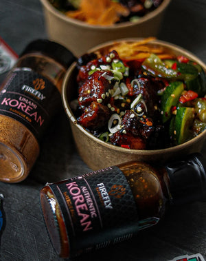 Firefly Korean BBQ Sauce and Umami Korean BBQ Rub next to a bowl of saucy grilled meat and vegetables, showcasing versatile use.