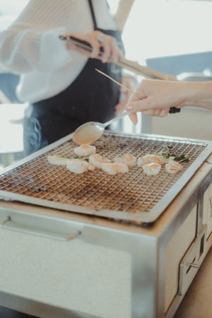 People grilling seafood on the Kasai Konro BBQ Grill - Medium with stainless steel frame, demonstrating its use in social outdoor cooking settings.