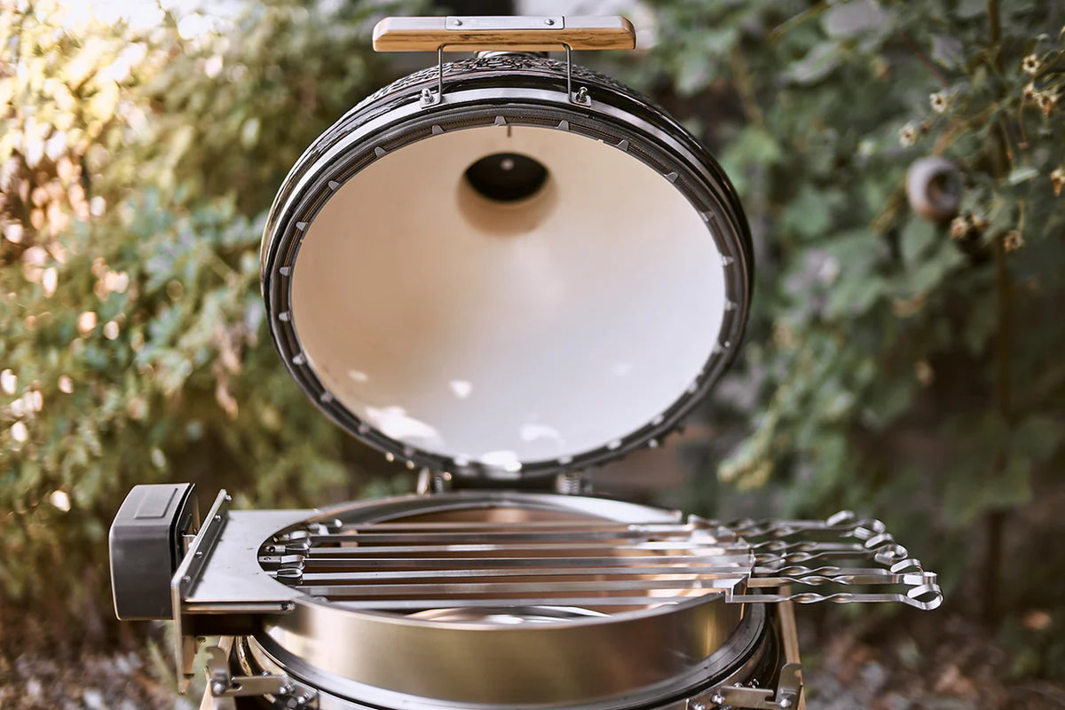 Portable grill with a lid open, showing the interior, against a blurred natural background.