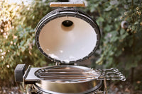 Portable grill with a lid open, showing the interior, against a blurred natural background.