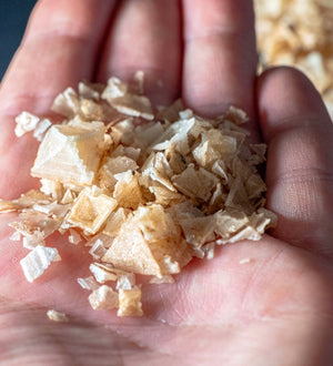 Hand holding Oak Smoked Greek Pyramid Salt flakes, showing the unique pyramid shape and texture of this gourmet seasoning.