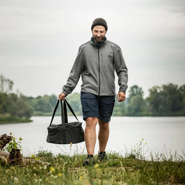 Man carrying a black Petromax transport bag with outdoor gear near a river