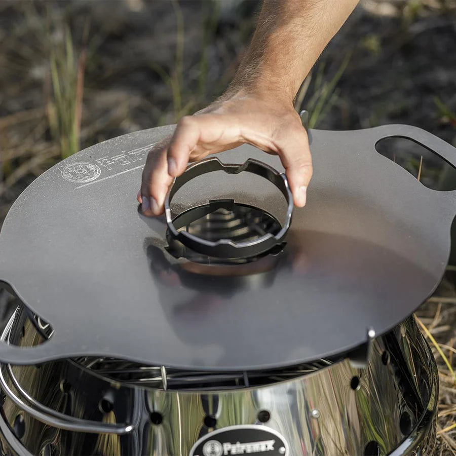 Person placing Petromax support ring on outdoor grill