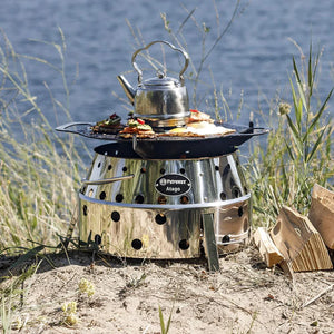 Petromax Atago grill plate in use outdoors by a lake, cooking with kettle and food on top of Atago grill for camping meals.