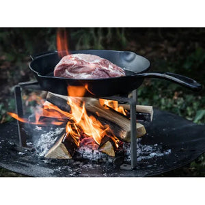 Petromax Cooking Stand in use with a Dutch oven over a wood fire, demonstrating its strength and stability for outdoor cooking.