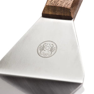 Close-up of Petromax Flexible Spatula with Long Handle showing engraved logo on stainless steel blade, highlighting premium outdoor grill accessory design.